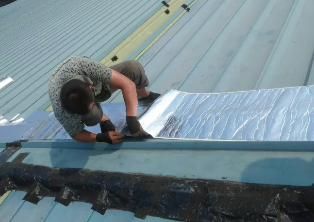 a worker applying butyl tape on roof top