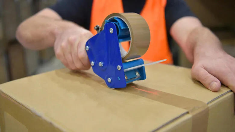 A worker sealing carton box with packaging tape dispenser